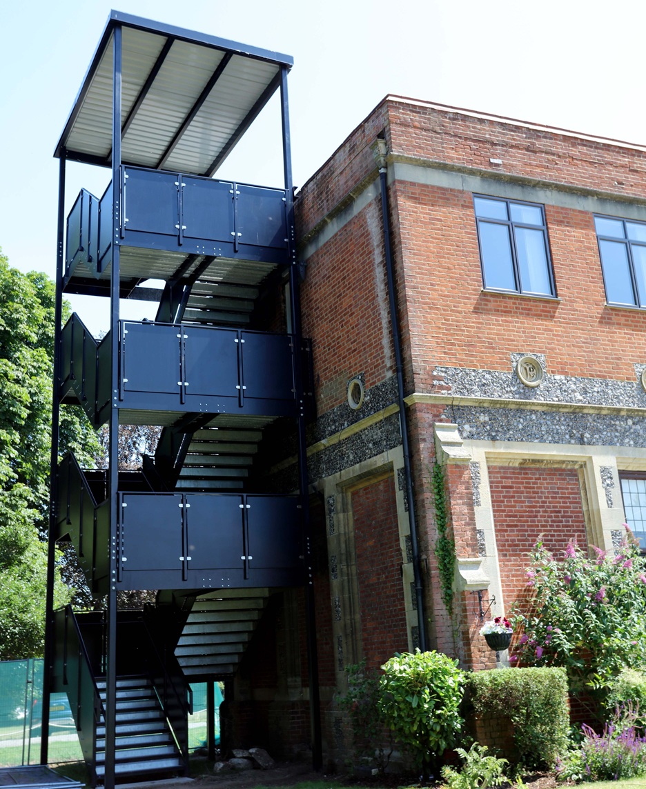 A multi-level, black metal external staircase with a roof attached to the side of a building