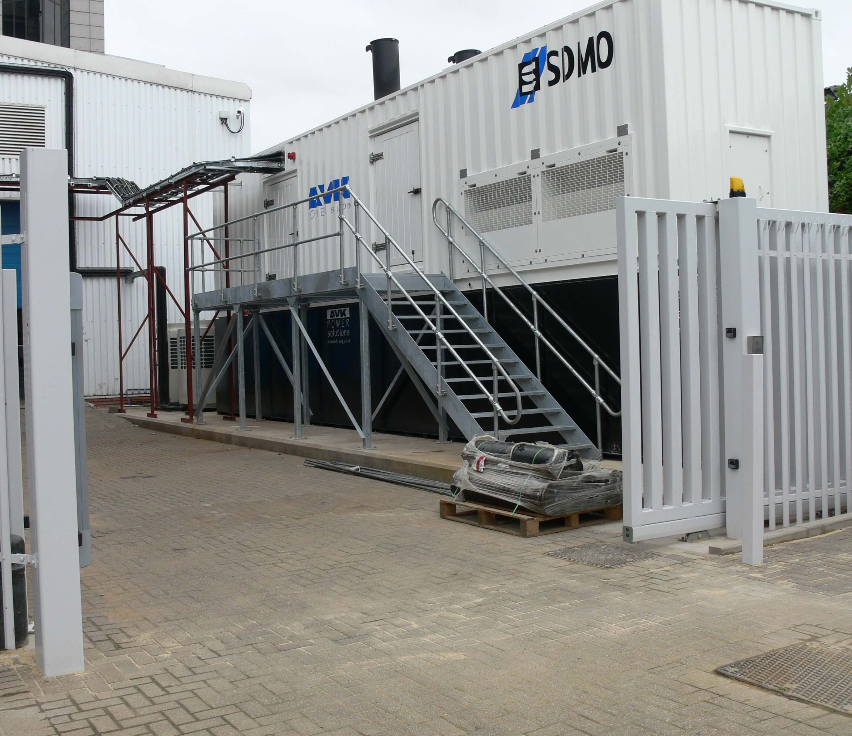A metal industrial walkway that leads to a doorway of a large white container.