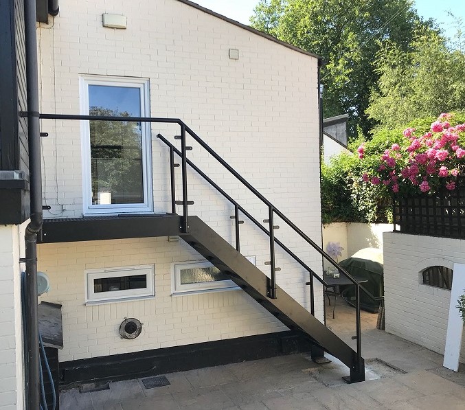 A black metal garden staircase with railings that leads to a second-story door.