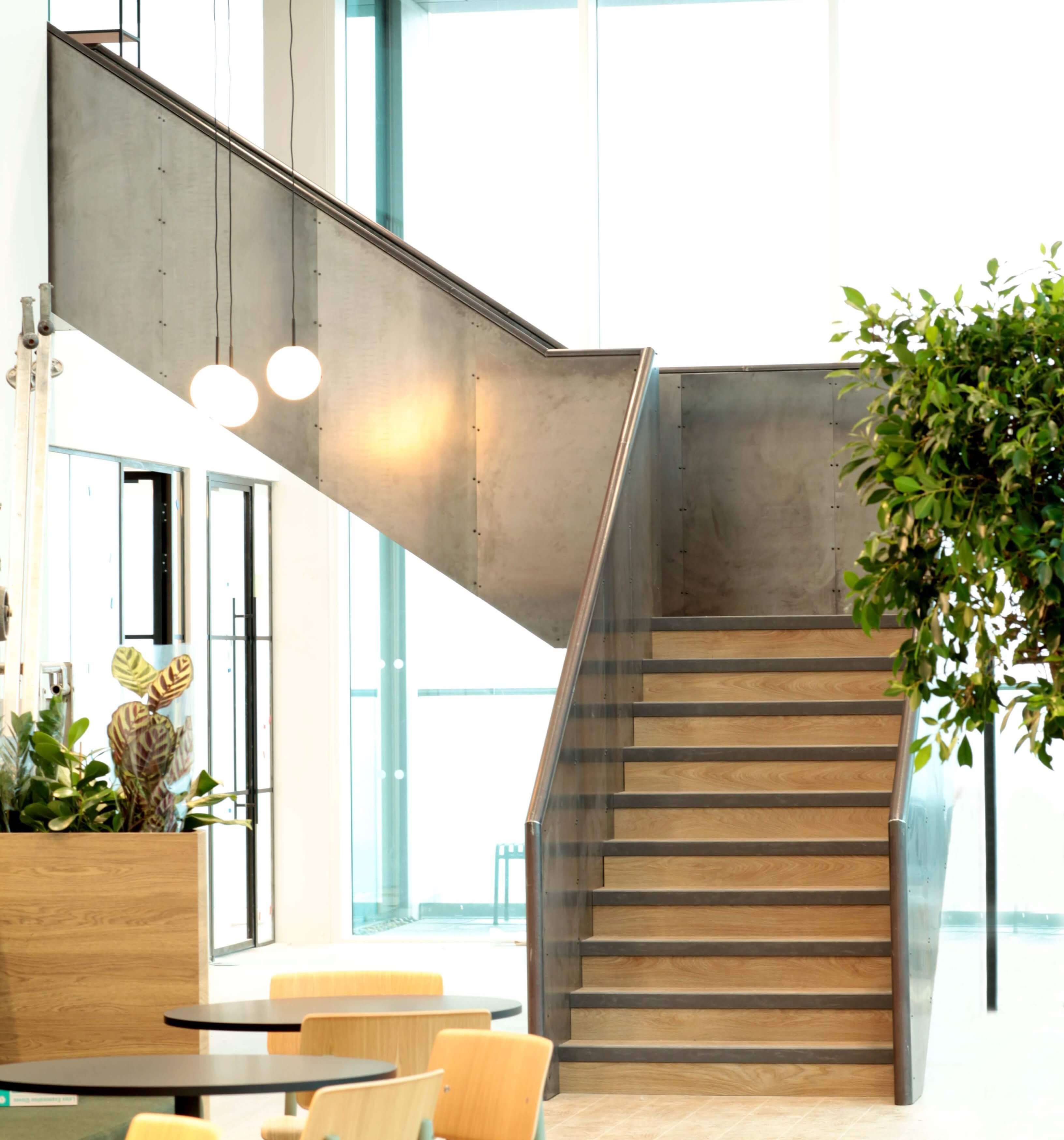 A modern internal staircase with wooden treads and a steel panel balustrade located in a business environment