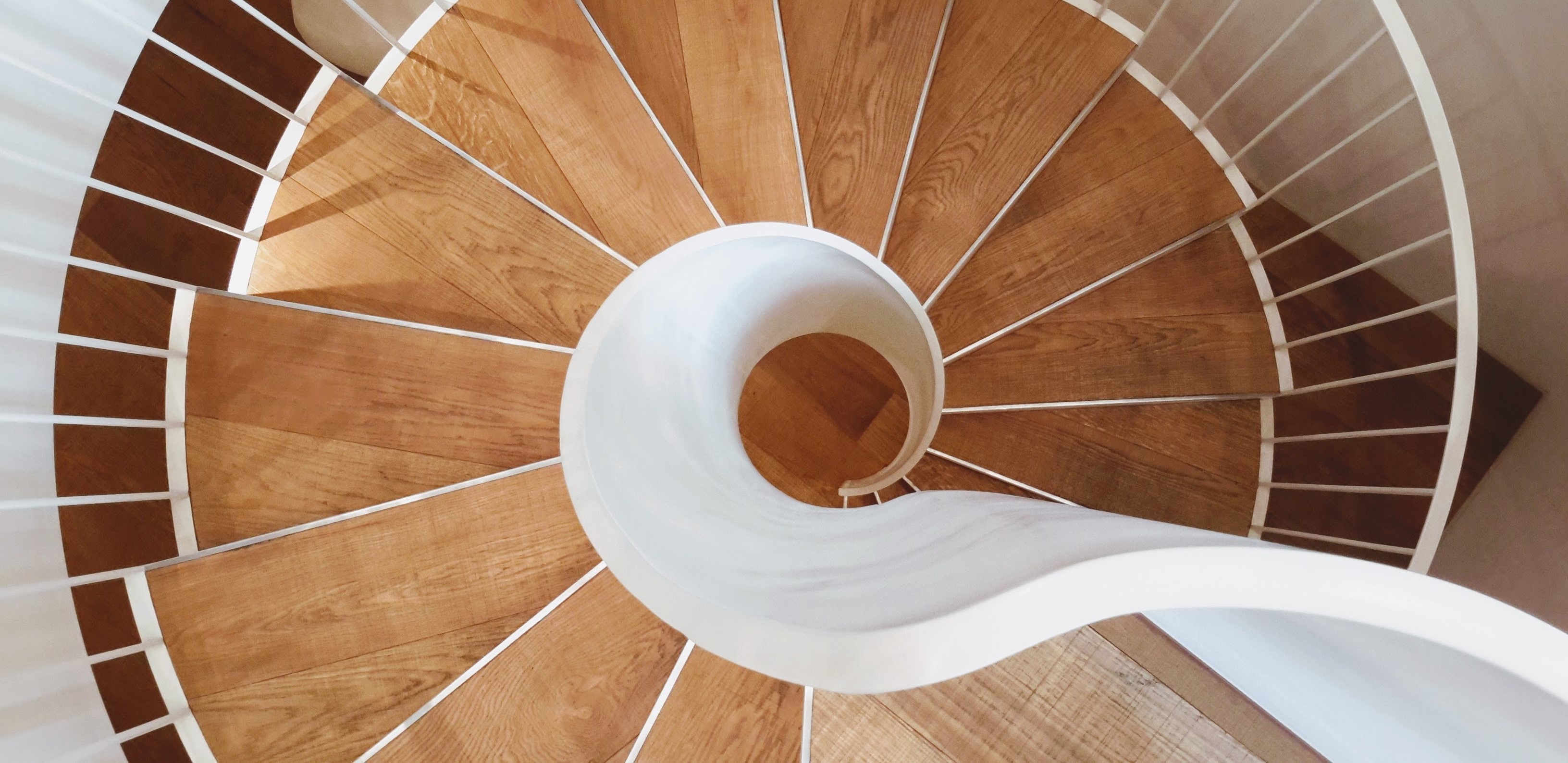A wooden tread spiral staircase viewed from above, with a white, metal swirling handrail.