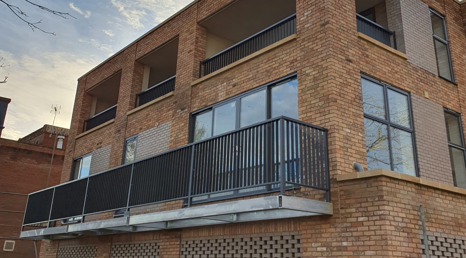 A modern apartment complex with steel balconies and black metal railings.