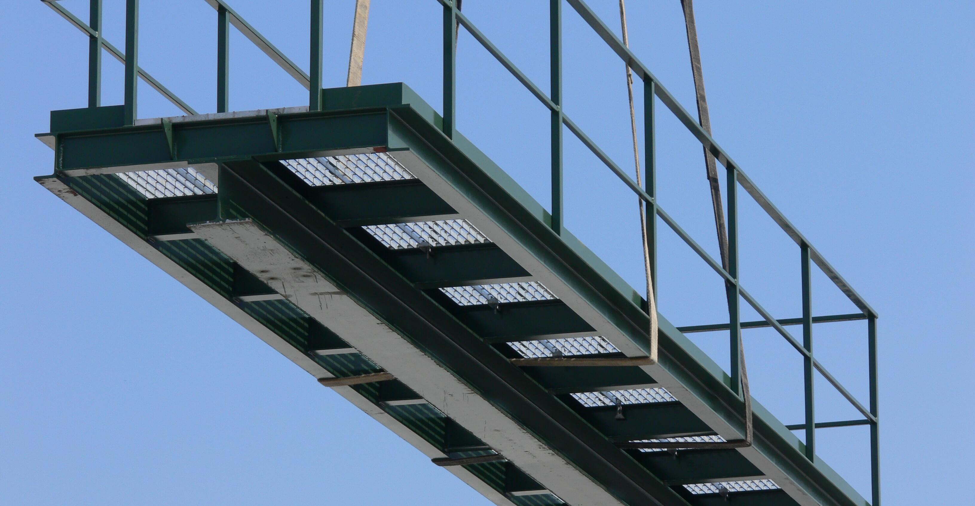 Green metal walkway with handrails suspended in the air with a crane